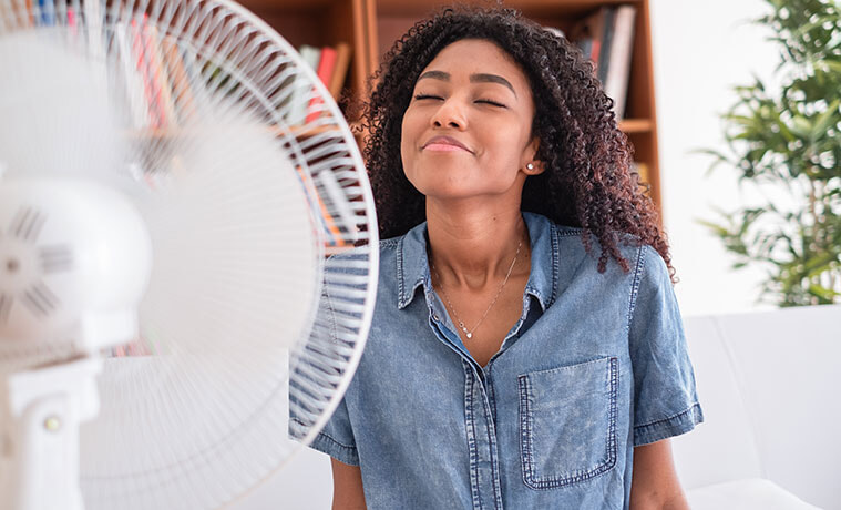 A smiling girl enjoys the cool breeze from a portable fan