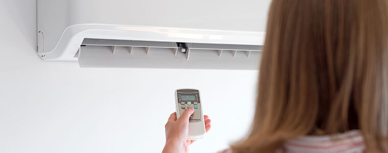 A woman aims a remote control at her wall-mounted air conditioner, turning it on to cool