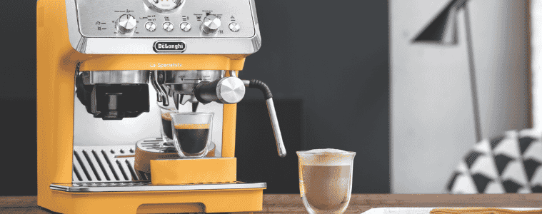 A DeLonghi LaSpecialista Arte Coffee Machine Yellow sits on a kitchen bench, a freshly brewed coffee in a glass sits beside it