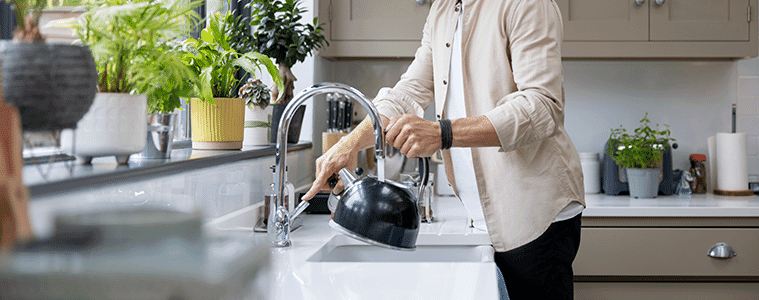 A man at the kitchen sink filling a kettle as water pours from an elegant gooseneck tap