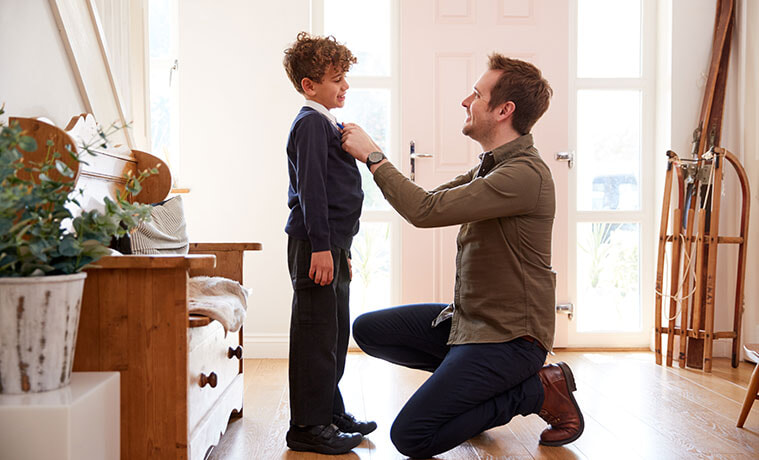 Kneeling man straightens his son's school uniform collar
