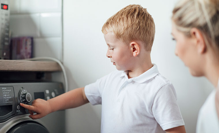 A mum shows her son how to use the washing machine in their laundry.