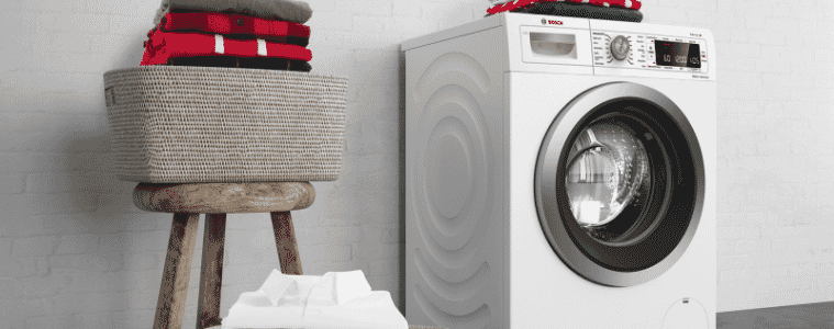 A Bosch washing machine with clean folded clothes on top of it sits next to a basket with clean folded clothes inside of it.
