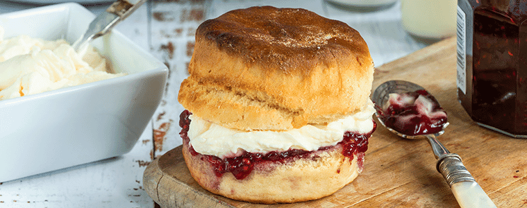 Scones with jam and cream on a decorative white plate with a bowl of fresh strawberries