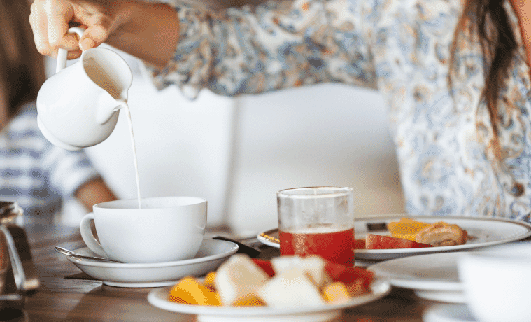 Woman pouring milk in mug from kettle. Breakfast time