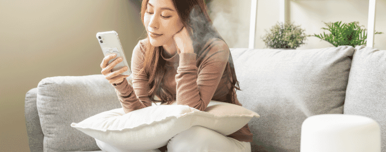 Woman using smartphone, enjoy aromatherapy steam scent from essential oil diffuser