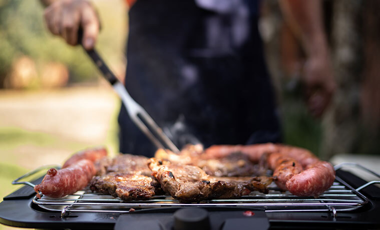 Man turns steaks and sausages on a sizzling barbecue grill