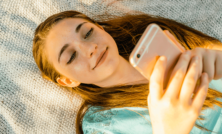 Young girl lying on her bed looking at her phone