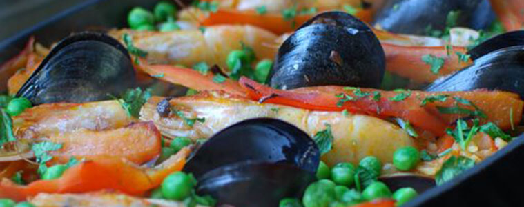 Mussels, prawns and seafood in a black bowl on a bbq grill with green peas