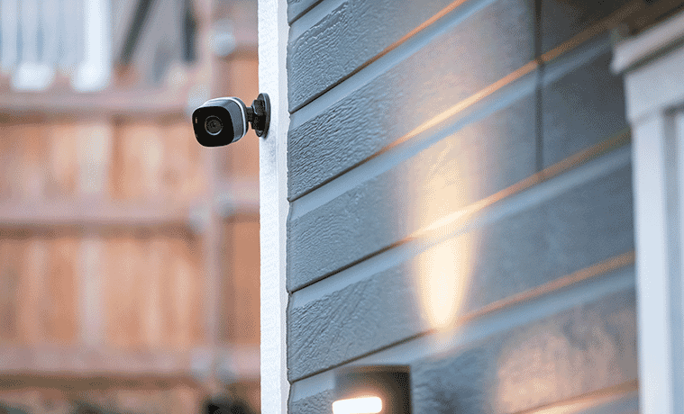 A discreet, black surveillance camera mounted high on an exterior wall of a house