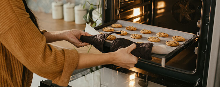 A woman removes a tray of cookies from the oven