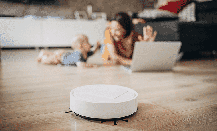 A mother and her baby play on the living room floor while a robot vacuum cleans the floor nearby