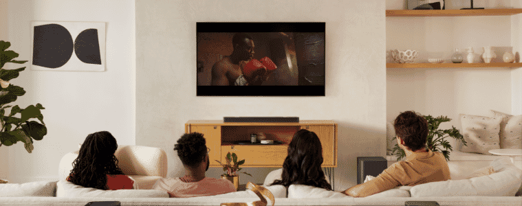 A group of people sit on a couch watching TV with a JBL Bar 1000 Soundbar