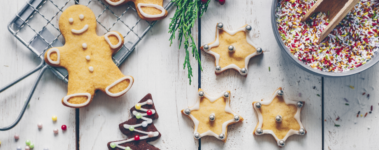 Gingerbread man shaped biscuits, star shaped cookies, hundreds and thousands, silver balls and pinecones on a white washed wooden board