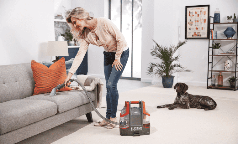 A woman uses a carpet cleaner to steam clean the couch to remove a stain in her living room