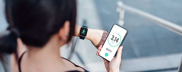 A woman in activewear checks fitness stats on her smartphone and synced smartwatch after a workout