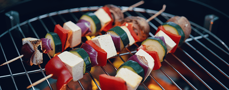 Close-up of vegetable and tofu skewers being grilled on an outdoor barbecue.
