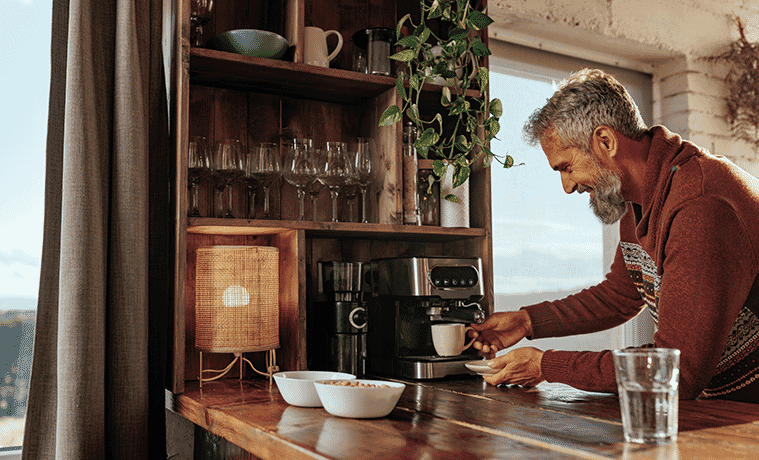 A man places a cup under the coffee machine on the timber benchtop in his rustic kitchen