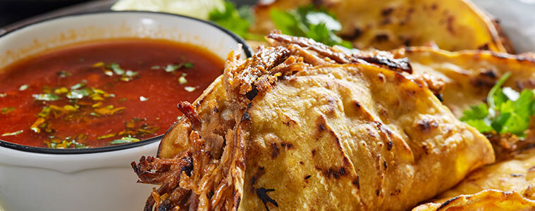 A crispy-fried birria taco next to a bowl of stew for dipping.