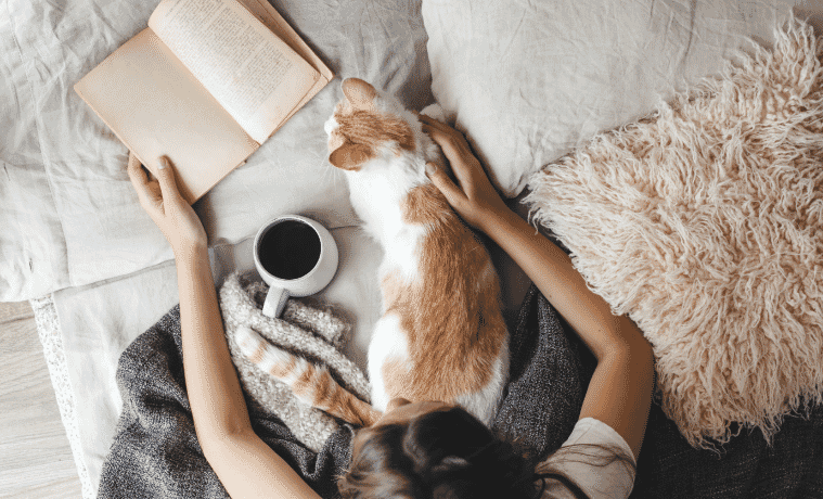 a woman sitting in bed with her cat and her book