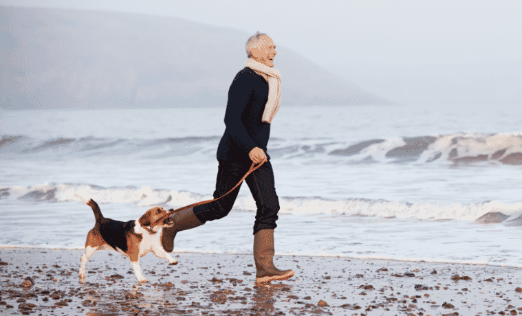 a man running along the beach in winter with his dog, wearing a scarf and boots 