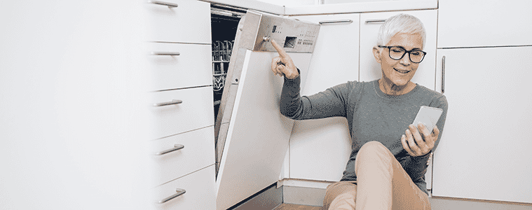 A woman sits on the floor near her Wi-Fi-connected dishwasher, to link it to her smartphone