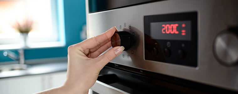 Close-up of a woman’s hand turning the knob on a wall oven to adjust the temperature.