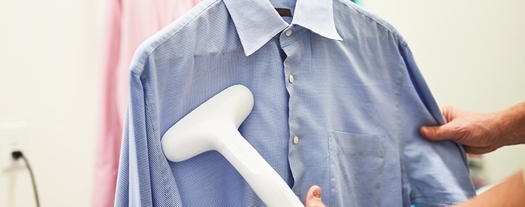 A close-up of a woman using a portable garment steamer on a linen shirt on a hanger. 