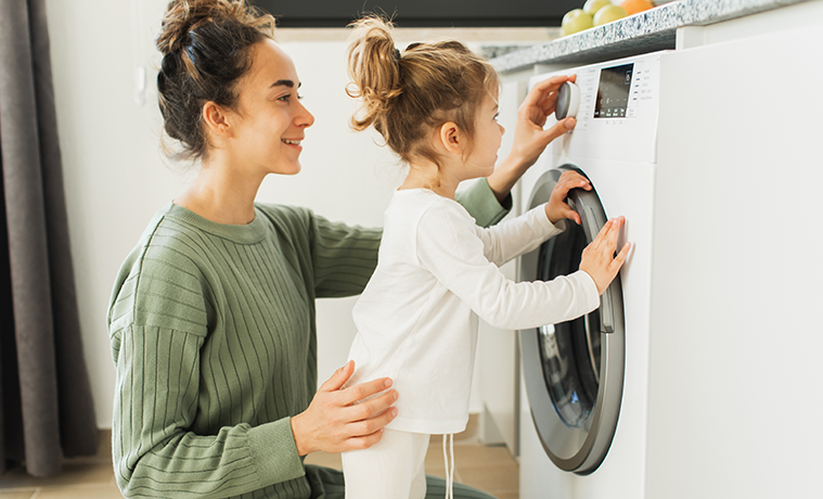 A mother putting washing in the washing machine whilst her daughter watches 