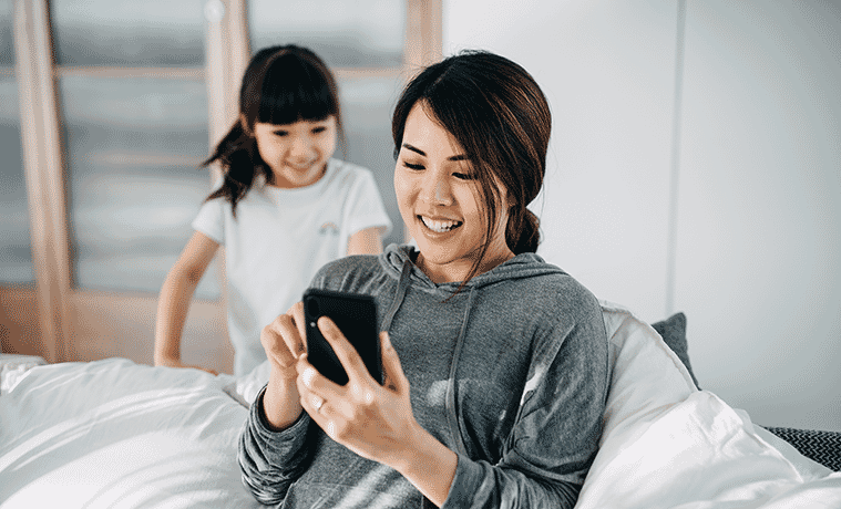 Busy mum checks her smartphone with her little girl looking over her shoulder.