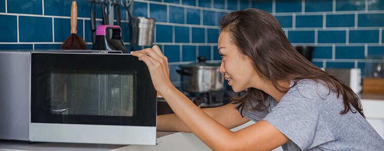 Woman opening the door of a microwave oven.