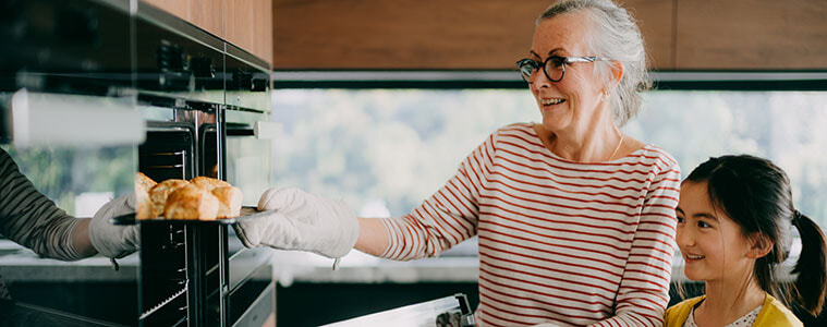 A grandmother and her granddaughter remove a tray of freshly baked scones from a wall oven.
