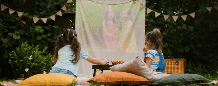 two girls sitting outside watching a movie on an outdoor projector 