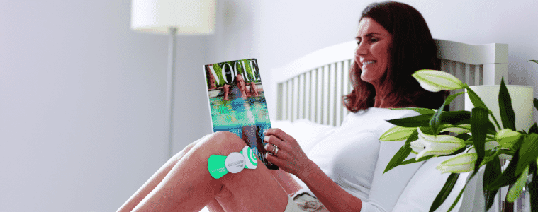 a woman sitting oh her bed reading a magazine using the Paingone Easy Wireless Tens Machine