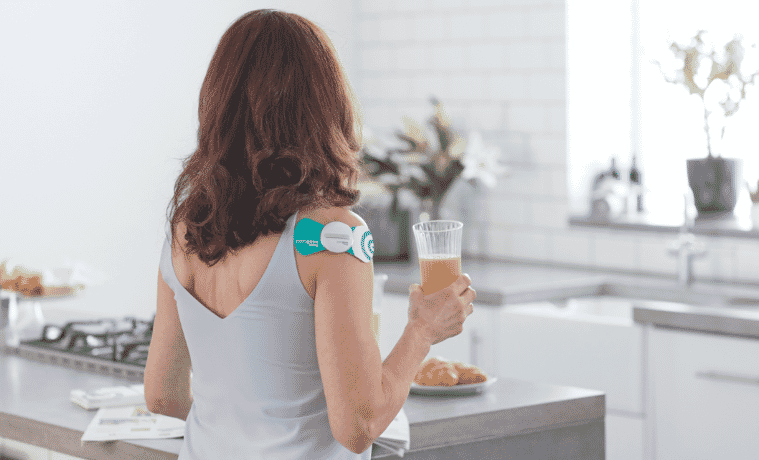 a woman standing in her kitchen drinking juice using her Paingone Easy Wireless Tens Machine