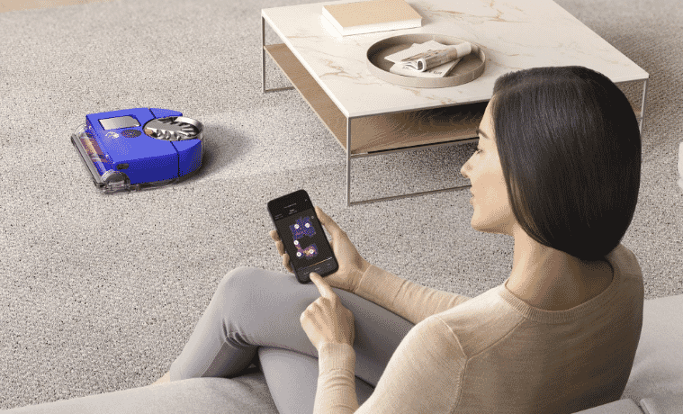 a woman sitting on her couch controlling her new Dyson robot vacuum from her phone 