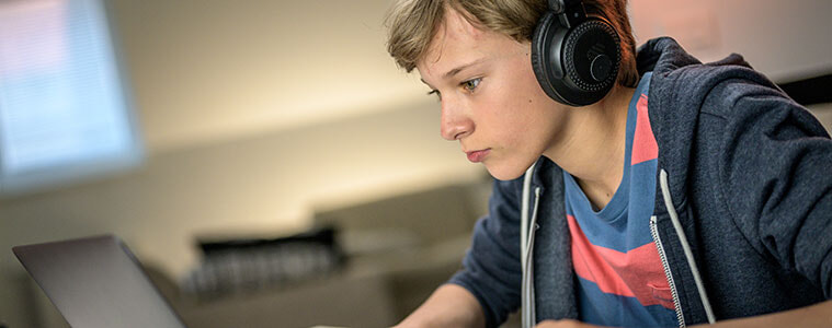 Boy with headphones plays a video game on his laptop at home.