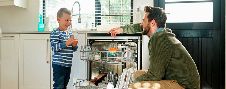 A young boy and his dad unload the dishwasher in a sunny kitchen