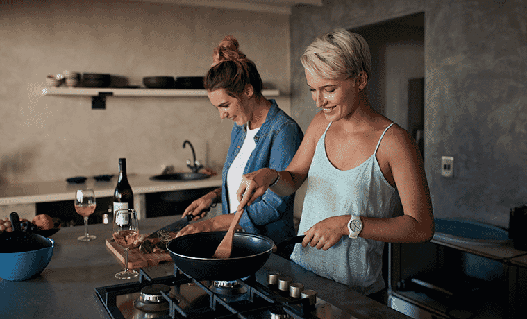 Two young women cook together in a loft apartment.