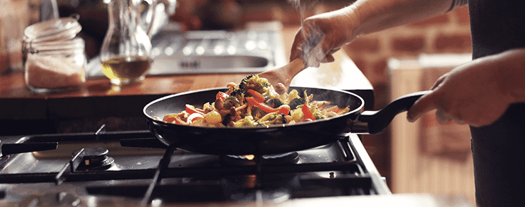 A woman cooks a stir fry in a fry pan on a gas cooktop at home.