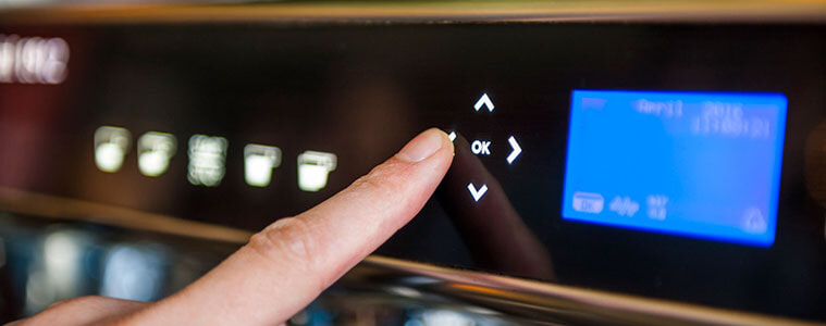 Close-up of a woman pushing a button on a digital panel on a coffee machine.