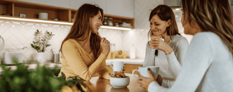 women sitting together drinking coffee in a kitchen 