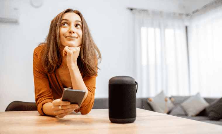 Woman at home with her smartphone and smart wireless speaker. 