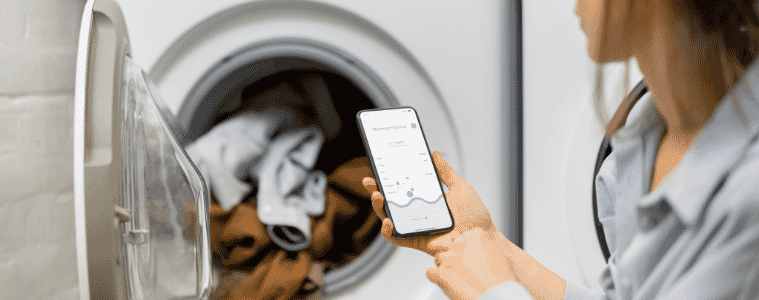Woman controls her Wi-Fi connected washing machine using a smartphone.