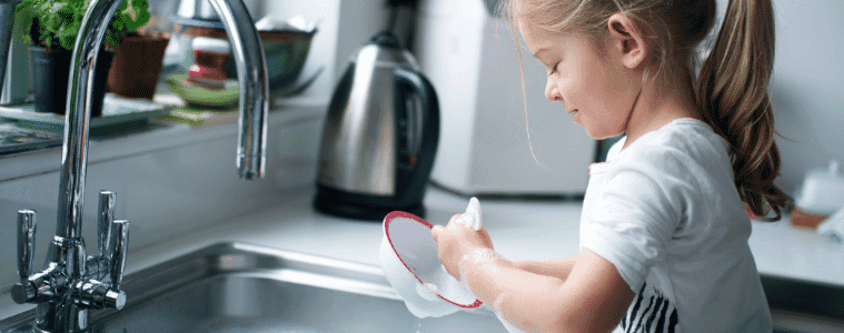 A little girl washes her bowl at the kitchen sink.
