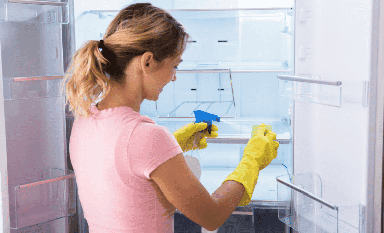 Woman wearing yellow gloves cleans inside her fridge.