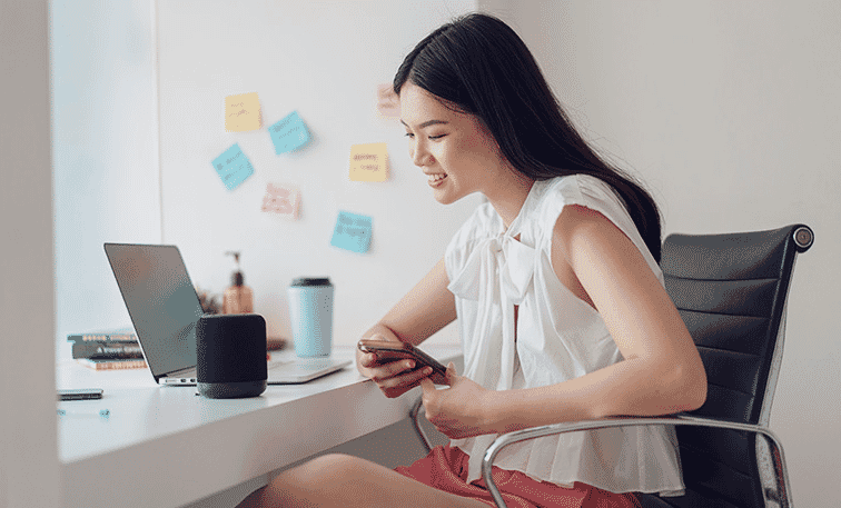 Young woman works from home with her smart assistant speaker and her portable laptop.