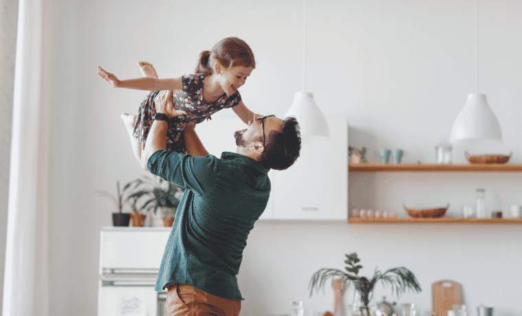 Father lifting daughter into the air as they laugh happily 