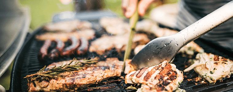 Close-up of a man using tongs to flip char-grilled chicken on a barbecue grill.