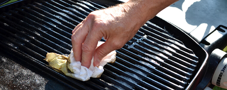 A man uses a brush to clean his barbecue grill plate. 
